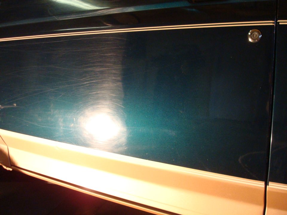 Teal vehicle side with cream stripe and numerous scratches. Door lock visible