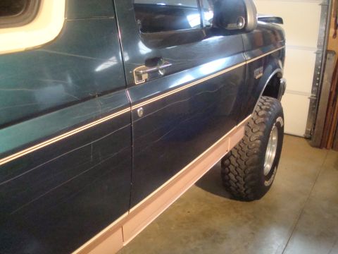 1995 Ford Bronco - Side view of a 1995 Ford Bronco, highlighting scratches on the dark green paint and a lifted suspension.
