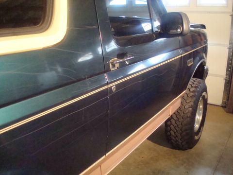 1995 Ford Bronco - Side view of a 1995 Ford Bronco, highlighting the dark green paint and beige trim, marred by many scratches.