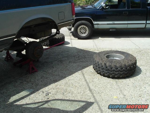 Silver truck on jack stands, black truck next to it, tire on ground