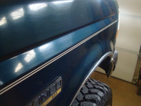 1995 Ford Bronco - Close-up of a dark teal 1995 Ford Bronco's fender and tire, revealing the "Bronco" emblem.