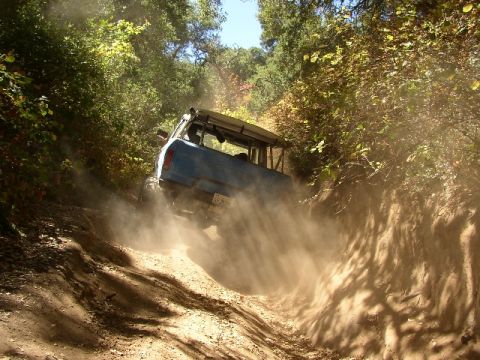 1989 Ford Bronco - A blue 1989 Ford Bronco navigates a dusty, wooded trail.