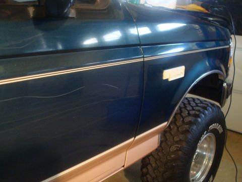 1995 Ford Bronco - This vehicle has extensive scratches on its dark blue paint, contrasting with its beige lower trim and pinstripes.