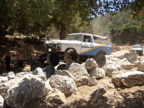 1989 Ford Bronco - Modified Ford Bronco navigates a rocky off-road course with spectators present.