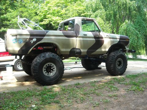 1979 Ford F-150 - A lifted pickup truck with a camouflage paint scheme sits on a driveway, with a boat visible to its left.