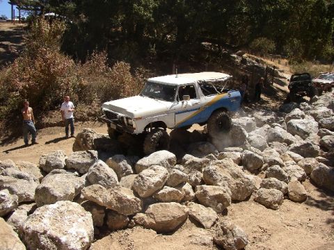 1989 Ford Bronco - This modified SUV is tackling a challenging rocky terrain, with spectators watching the action.