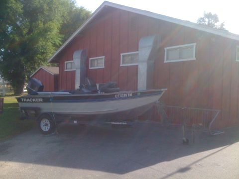 1996 Ford C-350 (Centurion Conversions) - A white and blue Tracker aluminum fishing boat with an outboard motor and pedestal seats sits on a Trailstar trailer beside a red board-and…