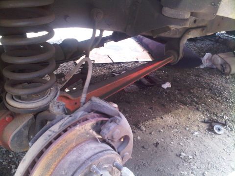 1986 Ford Bronco - Undercarriage view of a vehicle's suspension system, including the brake assembly and a red-painted control arm.