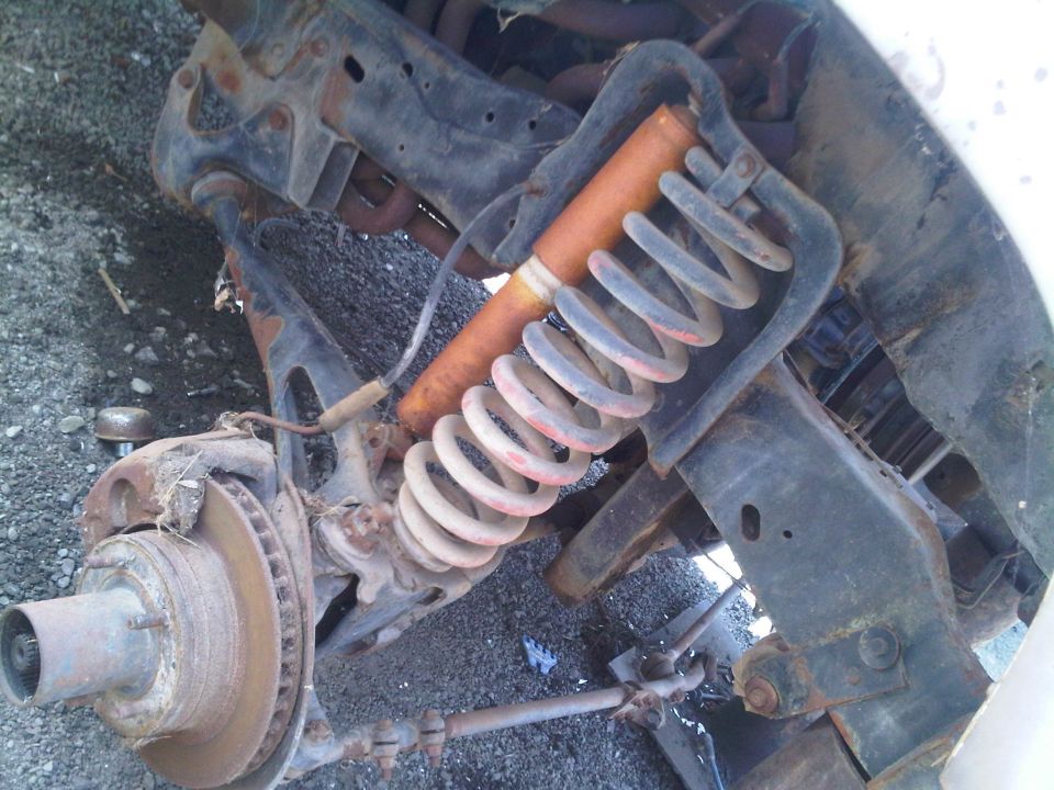 Rusty front suspension with coil spring and shock absorber, disc brake rotor visible