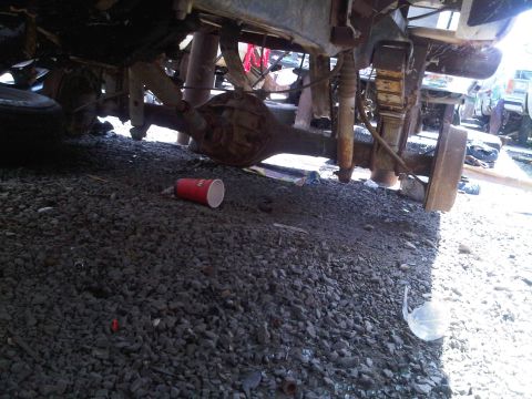 1986 Ford Bronco - The underside of a vehicle, focusing on the rear axle and suspension components, is visible in this junkyard scene.