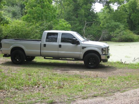 2008 Ford F-250 - A silver crew cab pickup truck is parked on a grassy area next to a pond with green algae.