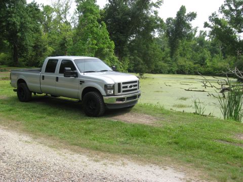 2008 Ford F-250 - A silver crew cab pickup truck is parked on a grassy area next to a pond covered in green algae.