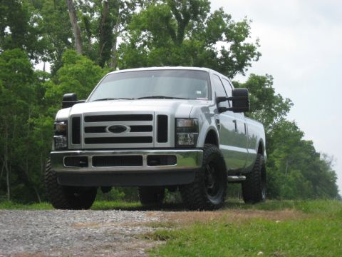 2008 Ford F-250 - A silver Ford F-250 pickup truck is parked on a gravel road, with trees lining the background.