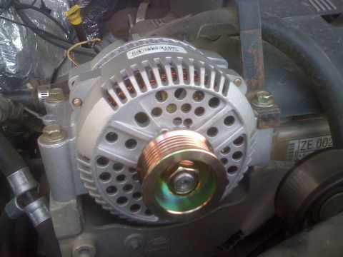 1996 Ford C-350 (Centurion Conversions) - Close-up of a freshly installed Ford alternator in an engine bay, its bare cast-aluminum housing and copper windings still clean and the go…