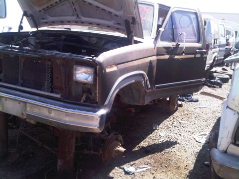 1986 Ford Bronco - Junkyard truck, likely from the early 1980s, with its hood and door open and missing front wheels.