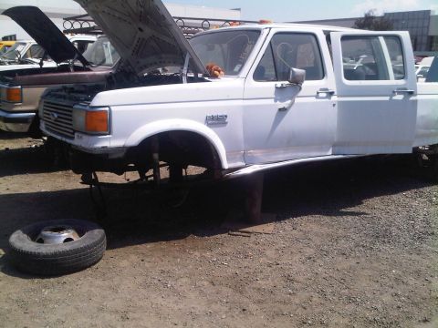 1986 Ford Bronco - Junkyard scene shows a white Ford F-350 truck missing its front wheels and with its hood open.