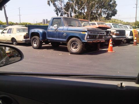 1986 Ford Bronco - A blue 1975 Ford F-Series pickup truck is parked in a lot with other vehicles.