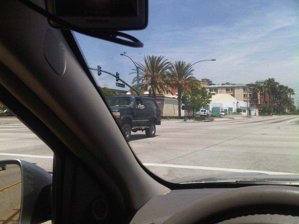 Dark SUV with lifted suspension driving through an intersection with palm trees and buildings in the background
