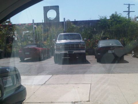 1986 Ford Bronco - A dark 1980s Ford truck is parked in front of a building, with other vehicles visible.