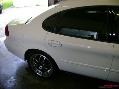 1993 Ford Taurus - Side view of a white sedan with aftermarket wheels, parked indoors.