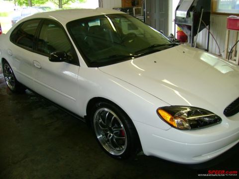 1993 Ford Taurus - This white sedan is parked indoors, showing off its custom wheels and tinted windows.