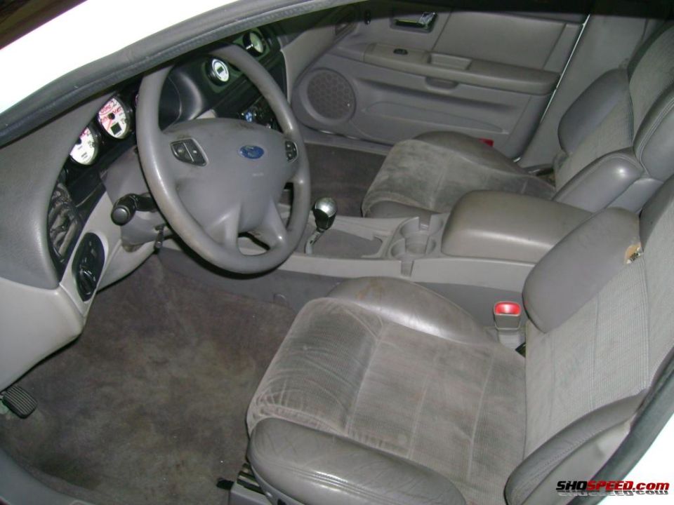 Interior of a car showing the steering wheel, dashboard, and front seats. The Ford logo is visible on the steering wheel