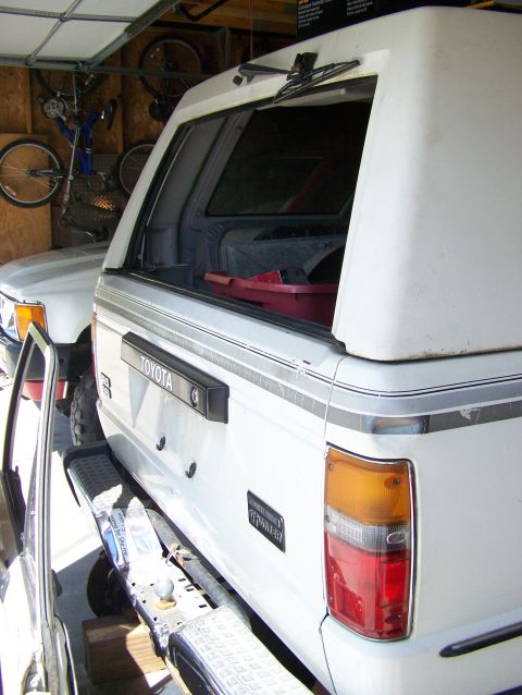 1988 Suzuki Samurai - A white Toyota pickup truck with a camper shell is parked in a garage next to another vehicle.
