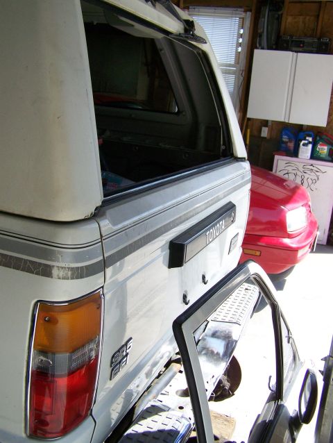 1988 Suzuki Samurai - The rear of a white Toyota pickup truck with a camper shell is visible, parked next to a red car.