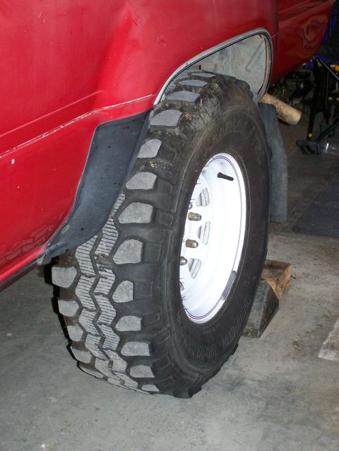 1988 Suzuki Samurai - Close-up of a red vehicle's rear wheel and tire, showing the tread pattern and fender flare.