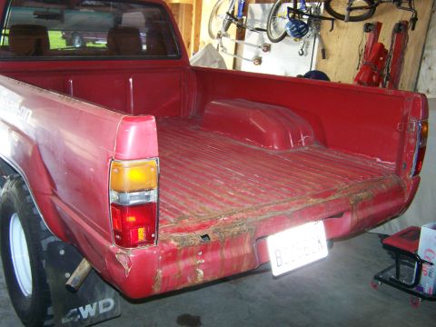 1988 Suzuki Samurai - This red pickup truck's bed shows signs of wear and tear, with a visible '4WD' marking on the mud flap.