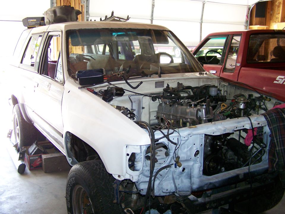 White SUV with engine removed, front view. Another red truck is visible