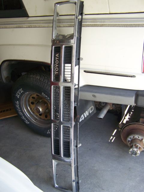 1988 Suzuki Samurai - A chrome Toyota grille is shown next to a white pickup truck, with one wheel removed.