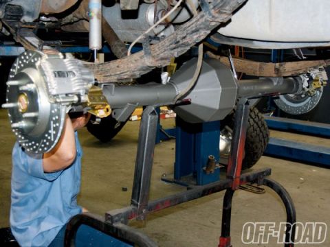 1990 Ford Bronco - A mechanic works on a vehicle's rear axle assembly, which features a Currie F9 housing and disc brakes.