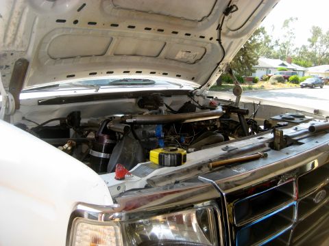 1996 Ford Bronco - The engine bay of a white truck is shown with the hood raised, revealing various mechanical components.