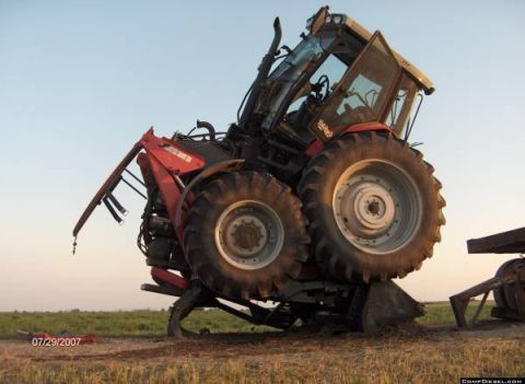 1994 Ford Bronco - A tractor has tipped onto its side in a field, with its large rear wheel propped up by an unseen object.