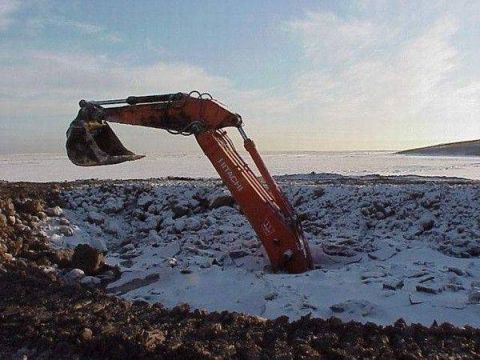 1994 Ford Bronco - An excavator is stuck in the snow and ice, with the arm extended over a hole.