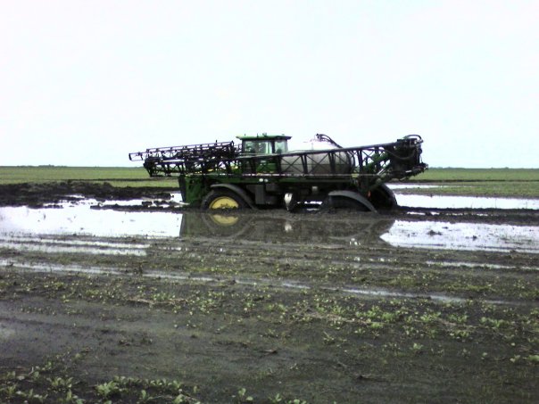 Green tractor stuck deep in muddy field with water covering the ground