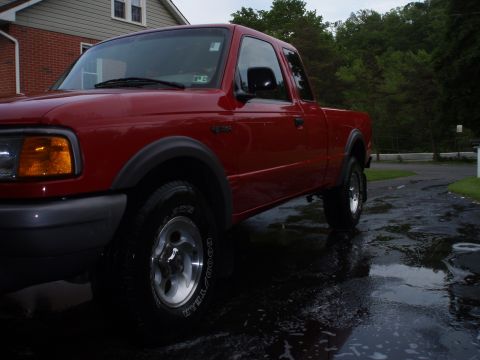 1997 Ford Ranger - Red 1997 Ford Ranger pickup truck parked on wet asphalt driveway with trees in background.