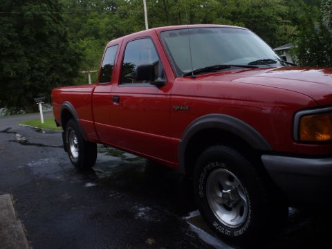 1997 Ford Ranger - Red 1997 Ford Ranger extended cab pickup truck parked on wet asphalt with trees in background.
