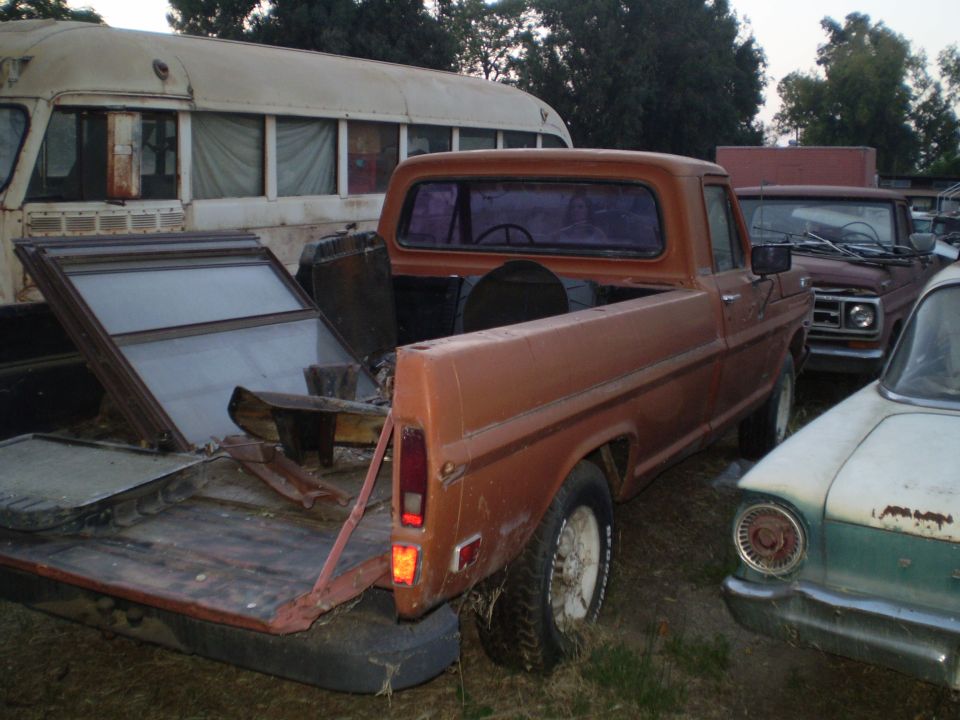 Faded orange vintage Ford long-bed pickup with tailgate down in a salvage yard