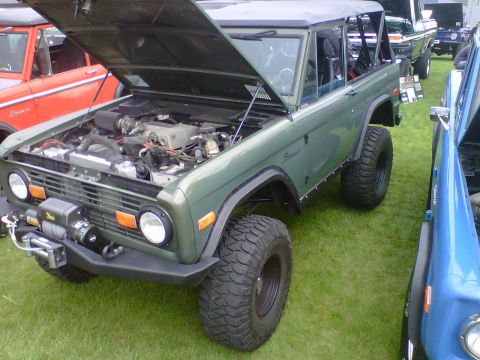 1995 Ford Bronco - Green Ford Bronco with hood open, displaying its engine and a winch mounted on the front bumper. Another Bronco is visible to the left.