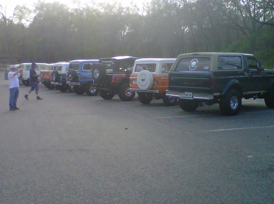 Line of Ford Broncos parked, rear view of green 1995 Ford Bronco prominent. Two people stand near the front