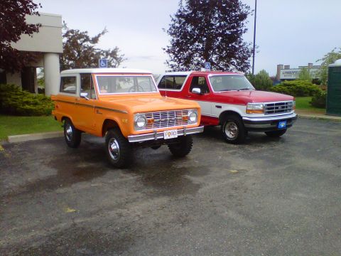 1995 Ford Bronco - Two Ford Broncos, one from the early 70s and a newer model, are parked side-by-side in a lot.