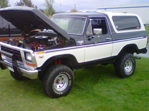 1995 Ford Bronco - This two-tone Ford Bronco features an open hood revealing its engine and a lifted suspension with off-road tires.