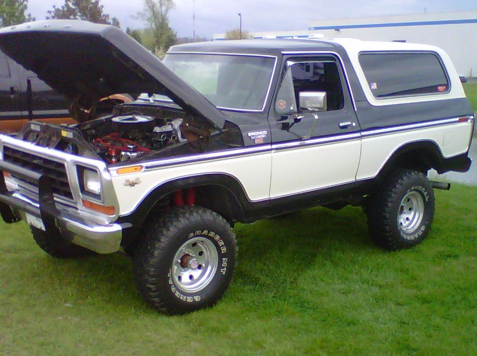 Two-tone black and white Ford Bronco with hood open, showing engine. Lifted suspension and off-road tires
