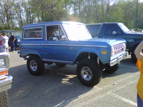 1995 Ford Bronco - A blue Ford Bronco is parked next to another vehicle under a bright sky.