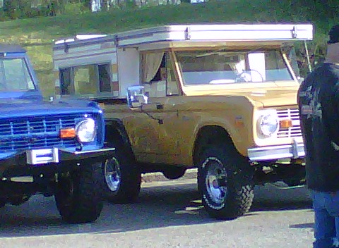 1995 Ford Bronco - Two Ford Broncos are parked side-by-side, one yellow with a camper top and one blue.