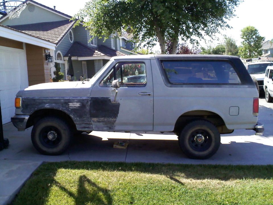 Gray 1987 Ford Bronco in driveway, primer on front fender, black top