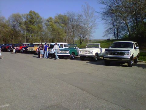 1995 Ford Bronco - A collection of Ford Broncos, including a white SUV and a green convertible, are parked outdoors on a sunny day.