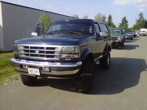 1995 Ford Bronco - Line of vehicles including a 1995 Ford Bronco with its driver's door ajar.
